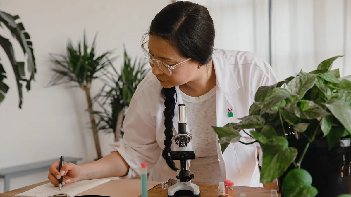 Female scientist conducting research and taking notes with microscope and plants.